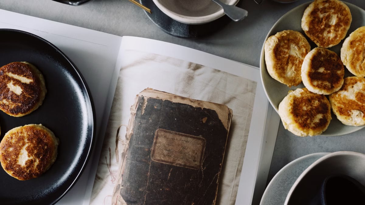 From above view of fresh hot buns served on plates near opened book on table with various kitchenware in light kitchen
